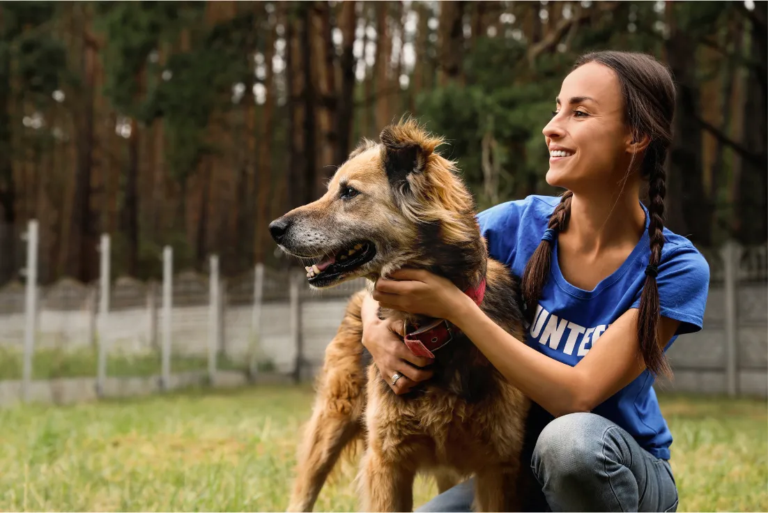 Smiling woman in a blue shirt hugging a shaggy rescue dog on a lawn