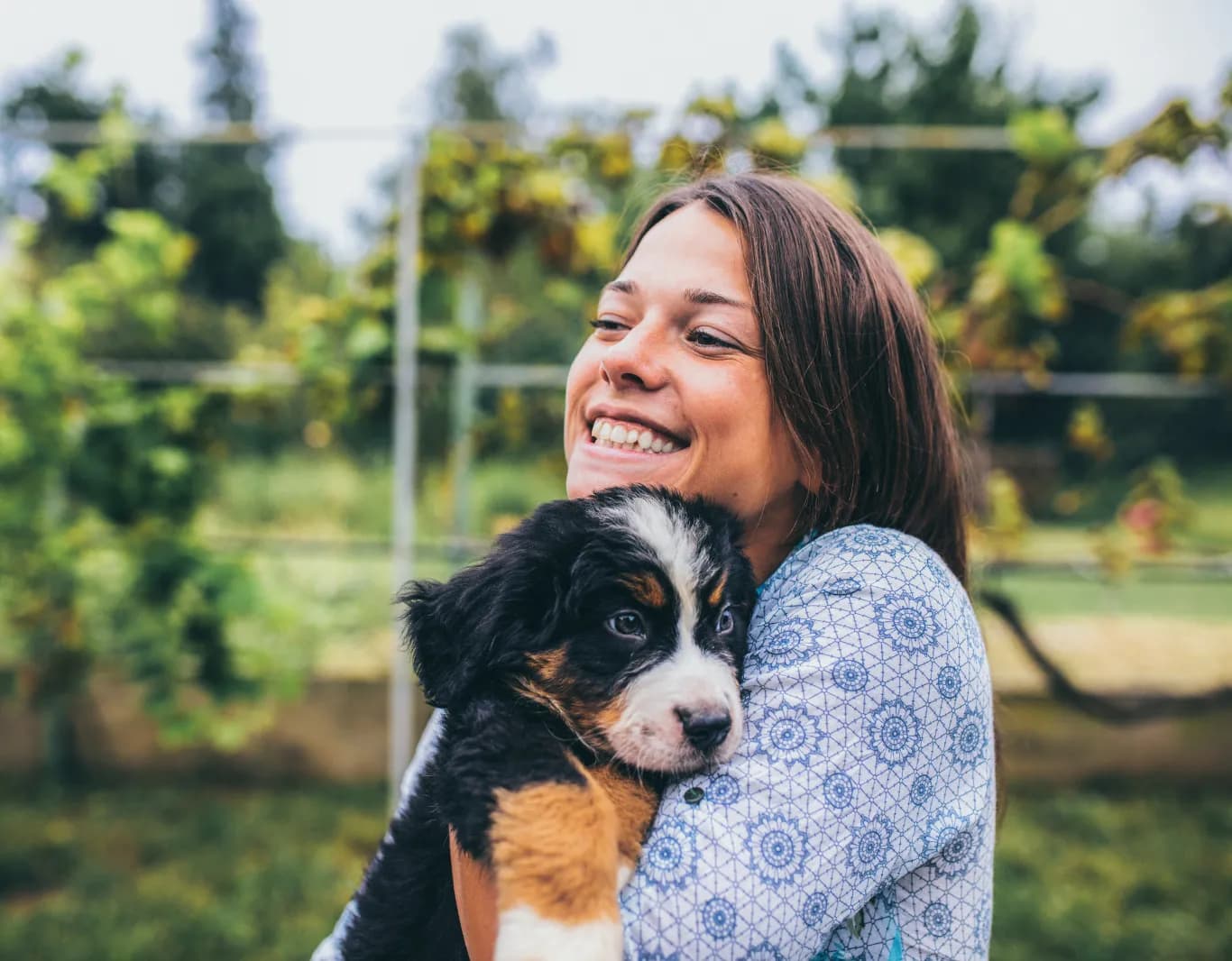 Smiling woman hugging a black, white and tan puppy outdoors