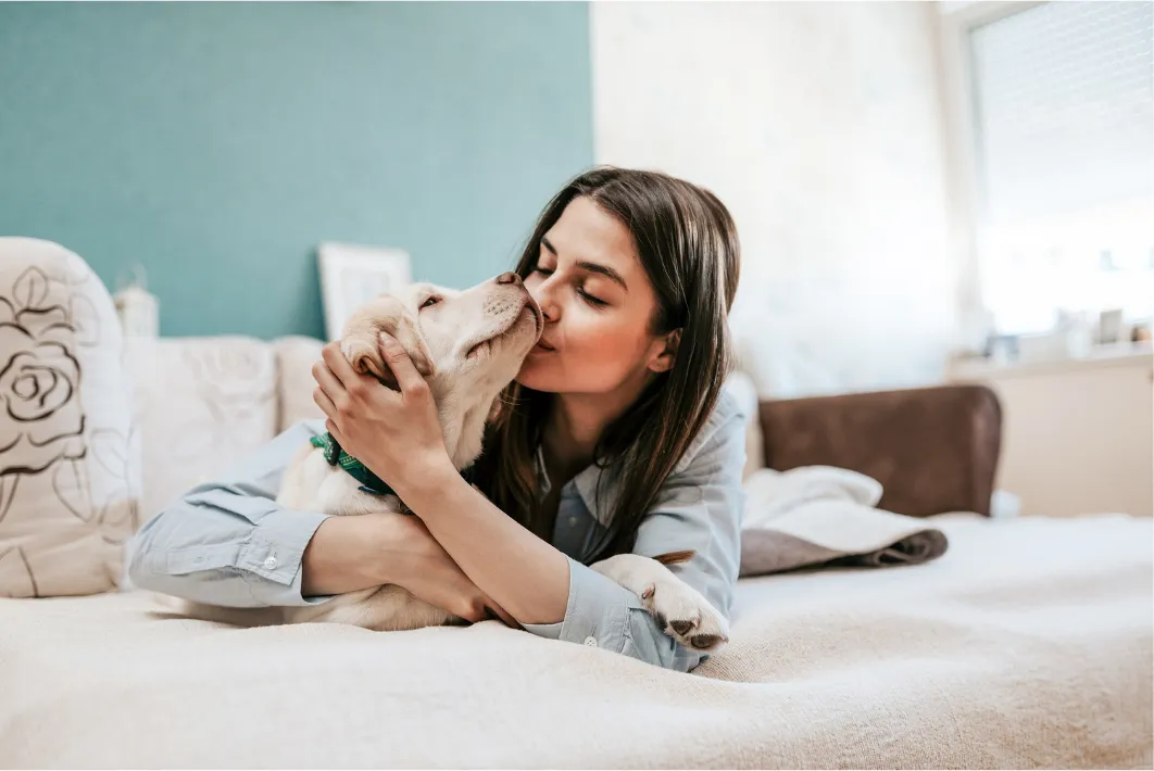 Woman lying on a bed and kissing her happy dog